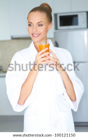 Stylish woman in a thick white towelling gown drinking a large glass of healthy orange juice