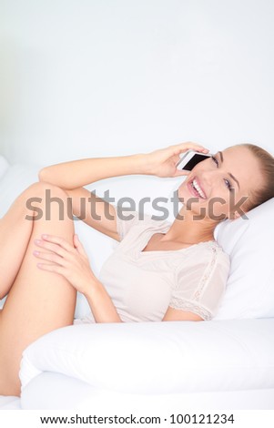 Beautiful woman sitting in an armchair laughing with friends over her mobile phone