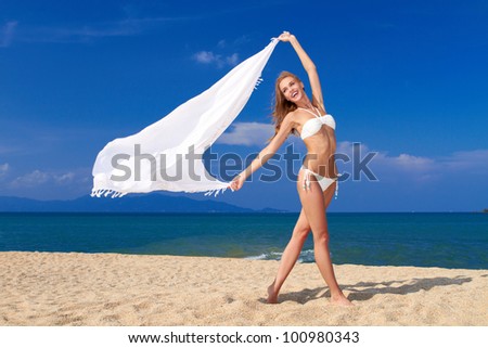 Smiling woman in white bikini holding white scarf against blue sky ,  on beautiful sandy beach