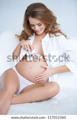 Young happy pregnant woman holding small baby shoes