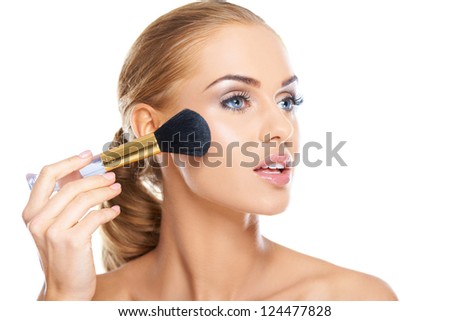 Beautiful blonde woman applying blusher or foundation powder to her cheek with a large soft cosmetics brush, beauty portrait isolated on white