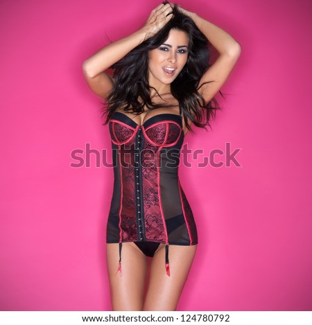 Sexy beautiful brunette woman with a busty figure posing in a corset against a pink studio background