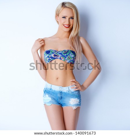 Happy sexy blond girl in short jeans and colorful bikini bra posing on white
