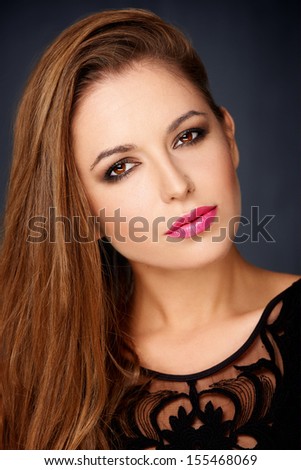 Sexy seductive woman with long brunette hair and red lipstick looking sideways at the camera with a sultry look over a dark studio background