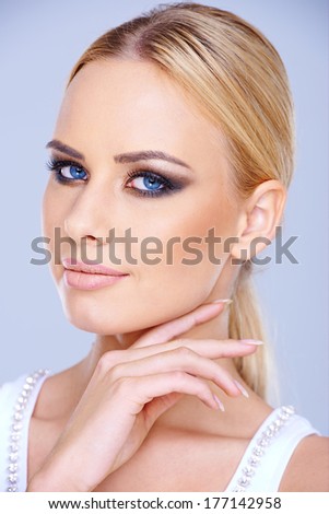 Smiling blue-eyed blond woman wearing dark eye makeup looking at the camera close up head portrait