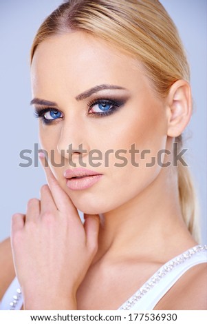 Beautiful blue-eyed blond woman wearing dark eye makeup looking at the camera close up head portrait