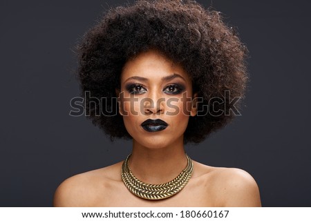 Beautiful exotic African American woman with a curly afro hairstyle wearing dark makeup and a gold choker looking directly at the camera with a serious thoughtful expression