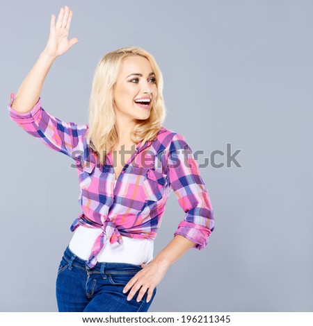 Beautiful young woman clowning around posing with on hand in the air and the other on her hip as she laughs and looks to the right of the frame  on grey with copyspace