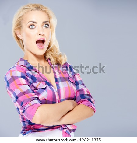 Beautiful woman with long blond hair standing with folded arms looking at the camera with her mouth wide open and a look of surprise  on grey with copyspace