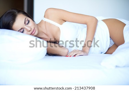 Attractive woman in her sleepwear having a restful sleep on a hot day with the bed clothes around her knees