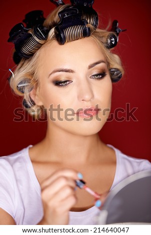 Beautiful young woman with her blond hair in curlers as she holds lipstick while looking in a mirror