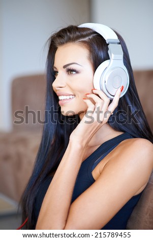 Beautiful young woman listening to music on a set of headphones as she gazes ahead with a lovely smile of enjoyment