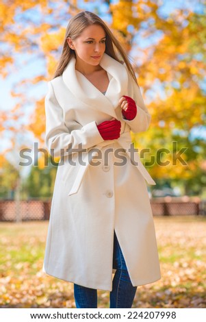 Attractive Serious Model in Elegant White Autumn Coat and Red Gloves Looking at Left Side Frame. Isolated on Nature Background.