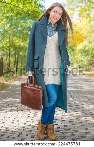 Pretty Young Woman Holding Leather Bag in Autumn Season Attire Posing at Pathway