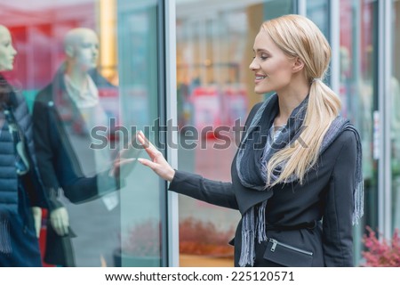 Happy attractive young woman window shopping standing outside a store window looking at the merchandise and smiling