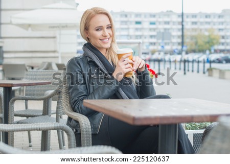 Smiling Pretty Blond Woman in Black Fashion Having Coffee Break at the Cafe Alone.