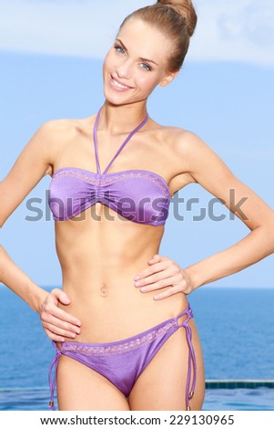 Close up Smiling Slim Woman Posing in Silky Sexy Violet Swim Wear at the Beach While Looking at the Camera.