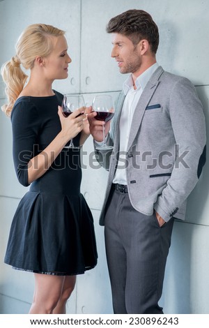 Young couple enjoying a romantic evening standing chatting over a glass of red wine in stylish evening clothes