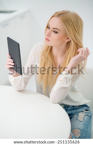 Close up Pretty Young Woman with long Blond Hair Sitting at the White Table  with Tablet Computer