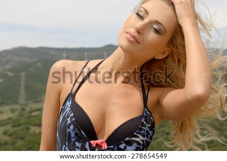 Attractive Blond Woman Wearing Bikini and Animal Print Dress and Hair Blowing in Breeze Standing on Hill near Wind Farm