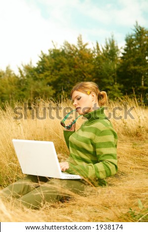Young business woman working on laptop computer on golden meadow at mountains outdoors