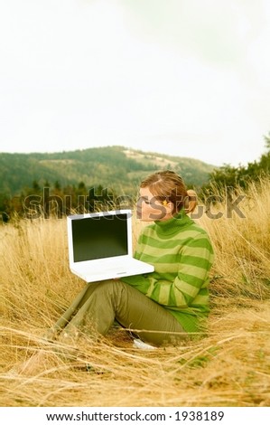 Young business woman holding laptop computer on golden meadow at mountains outdoors