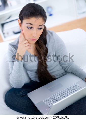 Worried young woman sitting on couch and working on laptop
