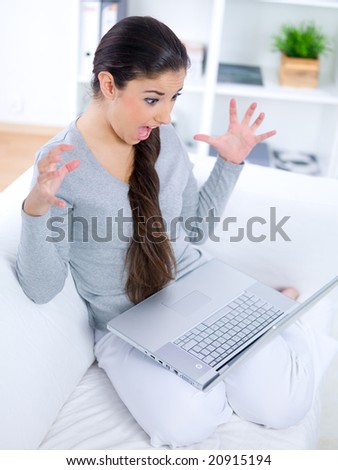 Thrilled young woman sitting on couch and working on laptop