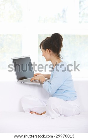 Young woman is on couch and working on laptop