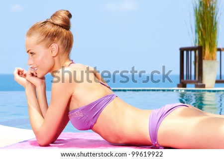 Gorgeous woman in a bikini taking sunbath close of an infinity pool