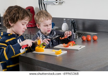 Two boys cutting some red and yellow peppers, used for cooking.