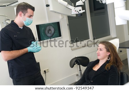 Dentist is explaining the patient what to do, picture of her teeth-problem in the background