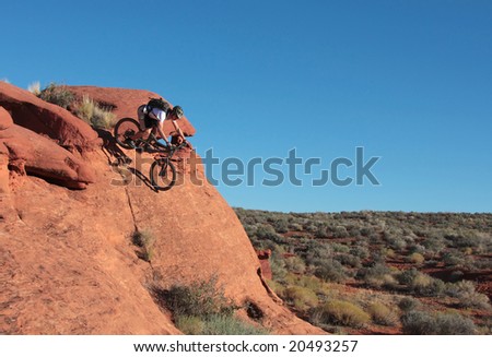 A rider drops down a steep sandstone feature in the Utah desert.