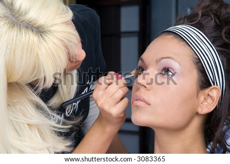 beautiful brunette girl model, while make-up before shooting session (professional make-up artist doing his job)