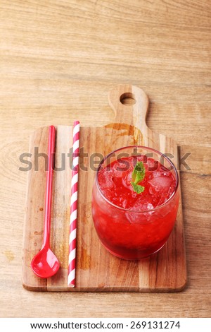 cold red soft drink from raspberry syrup and mint with red straw on wooden board