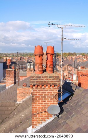 A brick chimney stack with red chimney pots and tv aerial with a view of surrounding rooftops.