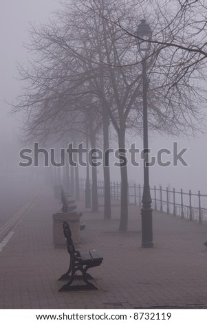 Line of benches and trees disappearing into the fog on a cold and misty morning near the River Dee in Chester UK.