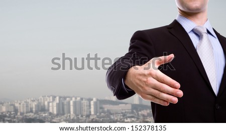 Portrait of young business man extending hand to shake over a cityscape