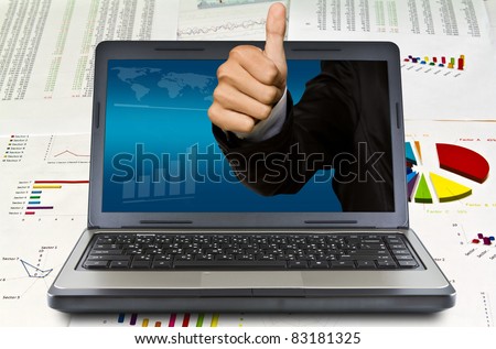 Business hand thumps up come out of the laptop screen on financial Graphs