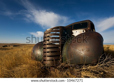 vintage truck abandoned and rusting away in the prairies, ghost town in the background