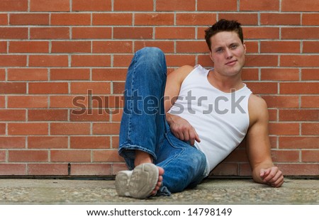 A fit male model leaning against a brick wall