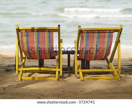 Two yellow and red lawn-chairs on the beach. Shallow depth of field with the background sea out of focus.