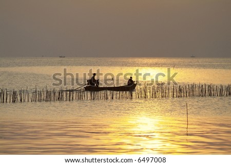 Silhouette of small boat at sea late in the afternoon with golden sunlight. Shallow depth of field with boat in focus. Photo taken in Thailand.