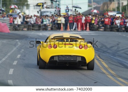 Rear of racing car braking before a 90 degree turn. Spectators in the background out of focus.