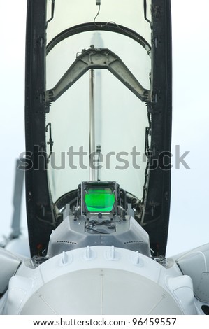 Front view of the open cockpit of a fighter jet with green head-up display.