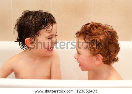 Brothers having fun at bath time splashing around in the water.  They are both enjoying themselves as they are splashing around and getting themselves cleaned before bedtime.