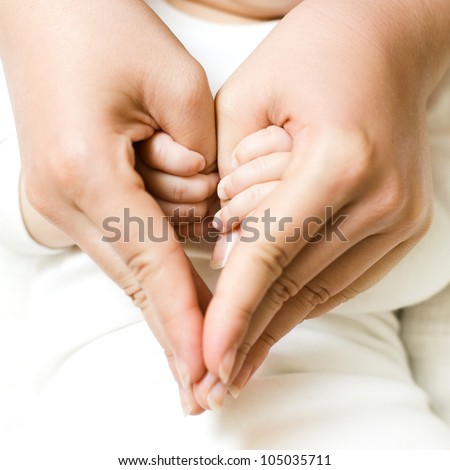 Baby holding mother finger and together form a heart shape by hand.