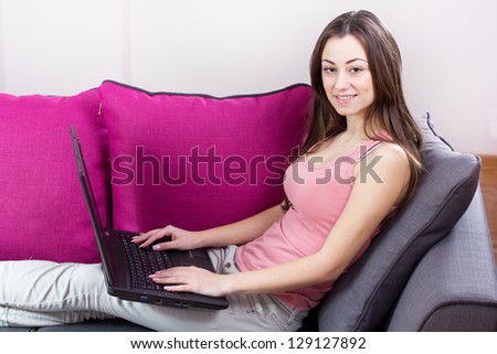Happy teenage girl relax on sofa using laptop at home.