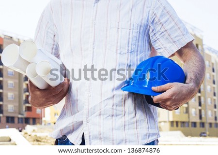 Closeup of construction worker holding project and blue hard hat,