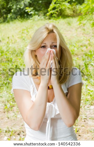 Young woman blowing nose outdoor, pollen allergy,